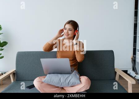 Eine Frau fühlt sich völlig entspannt, während sie mit ihren Kopfhörern sitzt und Musik auf ihrem Laptop hört. Stockfoto