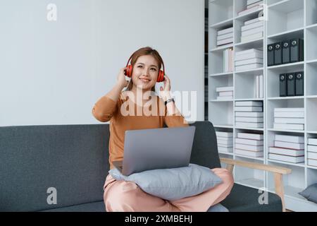 Eine Frau fühlt sich völlig entspannt, während sie mit ihren Kopfhörern sitzt und Musik auf ihrem Laptop hört. Stockfoto