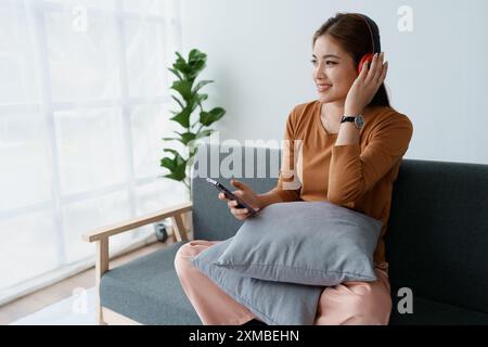 Eine Frau fühlt sich völlig entspannt, während sie mit ihren Kopfhörern sitzt und Musik auf ihrem Smartphone hört. Stockfoto