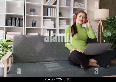 Eine Frau fühlt sich völlig entspannt, während sie mit ihren Kopfhörern sitzt und Musik auf ihrem Laptop hört. Stockfoto