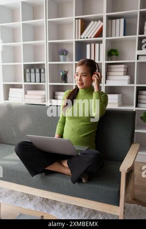 Eine Frau fühlt sich völlig entspannt, während sie mit ihren Kopfhörern sitzt und Musik auf ihrem Laptop hört. Stockfoto