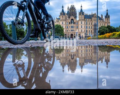 Schwerin, Deutschland. Juli 2024. Schloss Schwerin spiegelt sich in einer Pfütze. Am 27. Juli 2027 soll in Neu-Delhi (Indien) beschlossen werden, das Schwerin Residence Ensemble in die begehrte UNESCO-Liste des Weltkulturerbes aufzunehmen. Schwerin hofft, dass seine Aufnahme in das UNESCO-Weltkulturerbe den Tourismus ankurbeln und mehr internationale Aufmerksamkeit erregen wird. Quelle: Jens Büttner/dpa/Alamy Live News Stockfoto