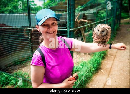 Porträt einer lachenden 36-jährigen russischen Frau mit Ural-Eulen (Strix uralensis) auf dem Arm sitzendem Vogel Stockfoto