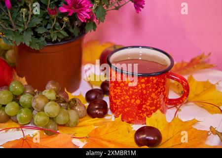 Orange Tasse Tee auf Ahornblättern mit Kastanien auf einem weißen Nachttisch Stockfoto