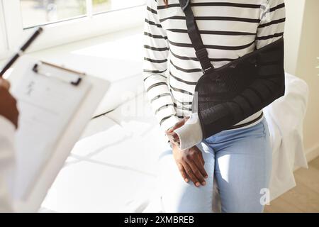 Eine Patientin mit einer Schlinge am verletzten Arm, die mit dem Arzt in der Klinik spricht Stockfoto