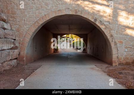 Ein Fußgängerweg unter einer Brücke führt zu einem üppigen Garten mit Blumen. Das luxuriöse Aphrodite Hills Hotel und Resort Gebäude mit wunderschönen Gärten Stockfoto