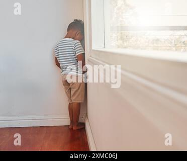 Traurig, Kind und Bestrafung durch die Wand Ecke für schlechtes Verhalten, Disziplin oder Stress in der Heimzeit. Junge, Rücken und freches Kind mit Angst vor Haustieren Stockfoto