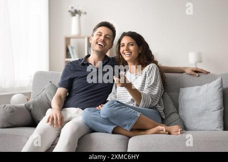 Lachende Pärchen sitzen bequem auf dem Sofa, vertieft in Fernsehen Stockfoto