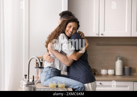 Eine hübsche verliebte Frau sitzt auf der Küchenarbeitsplatte und kuschelt Ehemann Stockfoto