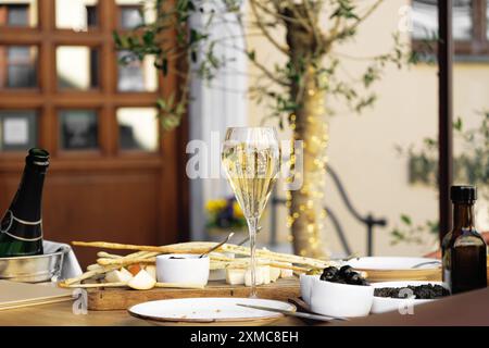 Elegante hohe Flöte mit gekühltem Sekt und verschiedenen Snacks auf einem eleganten, formellen Esstisch im Café oder Restaurant im Freien in der Fußgängerzone Stockfoto