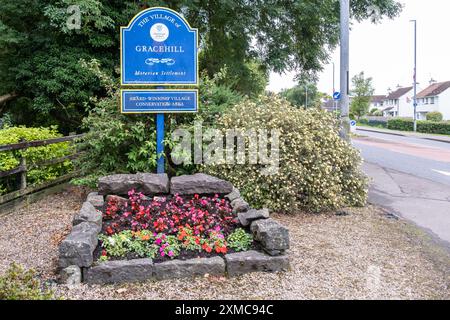 Gracehill, Nordirland - 26. Juli 2024: Die historische Siedlung der Mährischen Kirche gewinnt den Status des UNESCO-Weltkulturerbes, blaues Dorfzeichen und Blumen. Stockfoto