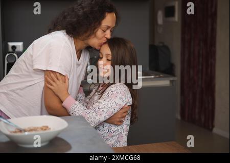 Ein zärtlicher Moment zwischen Mutter und Tochter, während sie sich in einer gemütlichen Küche umarmen und küssen. Warme Gefühle von Liebe, Fürsorge und familiärer Bindung werden dargestellt Stockfoto
