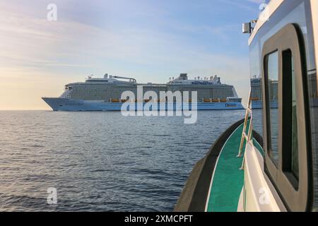 Nizza, Frankreich: Hafenpilotenboot nähert sich der riesigen MEERESHYMNE der Royal Caribbean, um den Seefahrer in Villefranche sur Mer zu besteigen. Ein einzigartiger Zwischenstopp für das größte Kreuzfahrtschiff dieses Jahr im kleinen Hafen der französischen Riviera. Nach der Sommersaison sollte das beeindruckende Schiff im Rahmen einer Umschichtung von Europa nach Singapur durch den Suez-Kanal segeln, aber nach Spannungen am Roten Meer und Drohungen mit Houthi-Raketen auf Schiffe, stattdessen wird sie ohne Passagier die Südspitze Afrikas erkunden, um Dubai und Asien zu erreichen. Quelle: Kevin Izorce/Alamy Live News Stockfoto