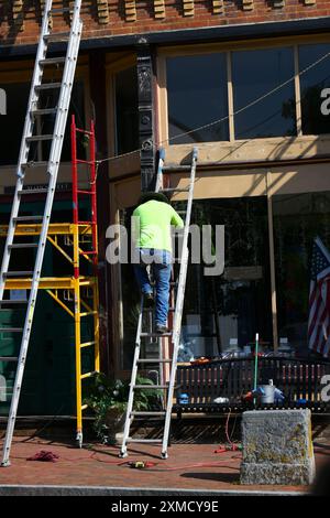 Man steigt die Leiter hinab, gestützt auf ein historisches Gebäude, an der Main Street, Jonesborough, Tennessee. Er hat Leitern und Gerüste. Er übermalt de Stockfoto