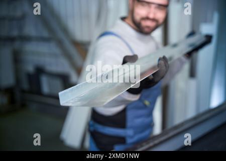 Ein Mann im Arbeitsanzug hält ein Aluminiumprofil in der Hand Stockfoto