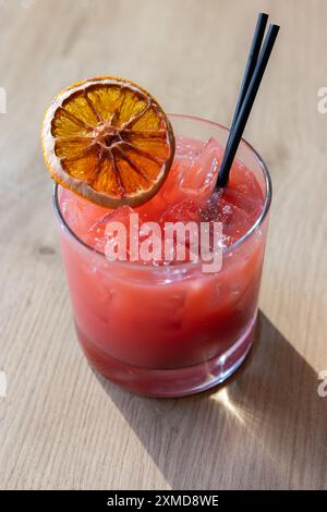 Ein Glas rosafarbenes Getränk mit einer Scheibe Orange darüber. Das Getränk wird in einem kurzen Glas mit schwarzem Strohhalm serviert Stockfoto