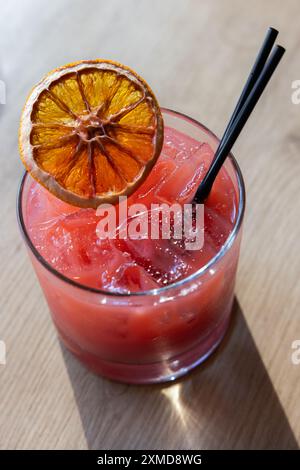 Ein Glas rosafarbenes Getränk mit einer Scheibe Orange darüber. Das Getränk wird in einem kurzen Glas mit schwarzem Strohhalm serviert Stockfoto