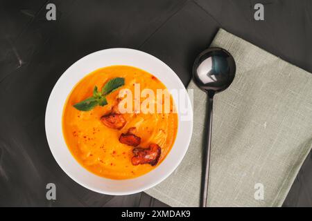 Kürbispüree Suppe mit Pfifferlingen und einem Minzzweig in einer weißen Schüssel auf einem schwarzen Tisch mit Serviette und Löffel. Hochwertige Fotos Stockfoto