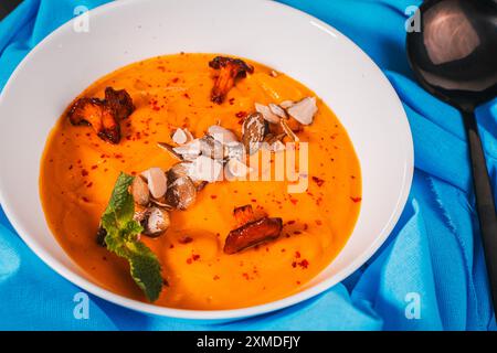 Kürbis-Karotten-Püree-Suppe mit Samen und Pilzen Chanterellen auf einer blauen Serviette. Hochwertige Fotos Stockfoto