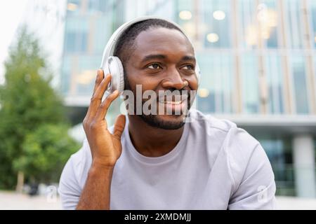 Musiksong-Konzept. Guter Start in den Tag. Glücklicher Afroamerikaner, der moderne Hit auf der Straße in der Stadt hört. Person Guy mit Kopfhörern genießen Sie Ihre Lieblingsmusik im Freien. Lebensfreude der Menschen Stockfoto