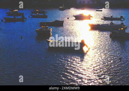 Eine Gruppe von Booten schwimmt im Wasser, die Sonne scheint auf dem Wasser. Die Szene ist friedlich und ruhig, die Boote reflektieren das Sonnenlicht Stockfoto