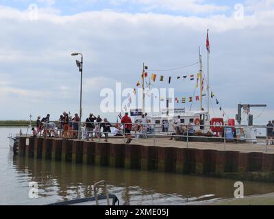 Sommerferien in Suffolk: bunting am Pier am Orford Quay mit Familien, die sich für die Orford Ness Fähre, Flussfahrten und Krabbenfischen versammeln. Stockfoto