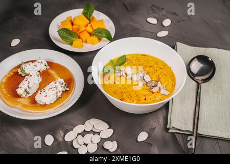 Diät, Gemüsecreme, Kürbissuppe mit Samen und Minze in einer weißen Schüssel und Hüttenkäse Quenelles mit Kräutern auf grauem Graphit Hintergrund. Autu Stockfoto