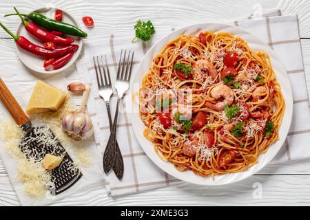 Garnelen fra diavolo mit Spaghetti, Tomatensoße, bestreut mit geriebenem Parmesankäse auf weißer Platte auf weißem Holztisch, horizontale Ansicht Stockfoto