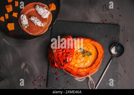 Traditionelle Gemüsesuppe, Kürbis- und Karottenpüree in einer gebackenen Kürbisschale auf einer schwarzen Glimmerplatte und Quark Quenelles mit Paprika und Kräutern Stockfoto