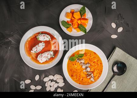 Diät, Gemüsecreme, Kürbissuppe mit Samen und Minze in einer weißen Schüssel und Hüttenkäse Quenelles mit Kräutern auf grauem Graphit Hintergrund. Autu Stockfoto