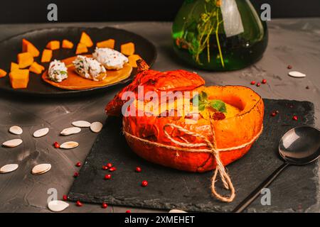 Gebackener Kürbis mit Suppe, Karotten und Kürbispüree mit Pilzen, Pfifferlingen und Minze auf einem schwarzen Teller und Hüttenkäsebällchen mit Paprika und ihr Stockfoto