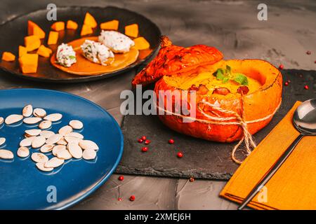 Gebackener Kürbis, gefüllt mit Gemüsepüree mit Pfifferlingen auf einem schwarzen Brett und einer blauen Platte mit Kürbiskernen. Hochwertige Fotos Stockfoto