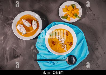 Kürbis-Karotten-Püree-Suppe mit Pilzen, Pfifferlingen und Minze in einer weißen Schüssel auf einem blauen Tuch auf grauem Hintergrund mit Hüttenkäsebällchen mit Stockfoto