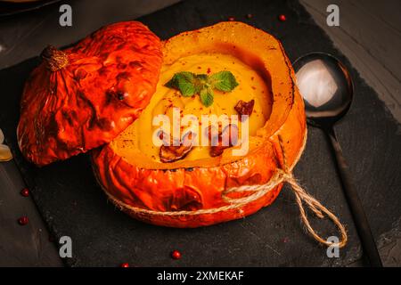 Gebackener Kürbis gefüllt mit Suppe, Gemüsepüree mit Pilzen, Pfifferlingen und Minze auf schwarzem Hintergrund, Nahaufnahme. Hochwertige Fotos Stockfoto