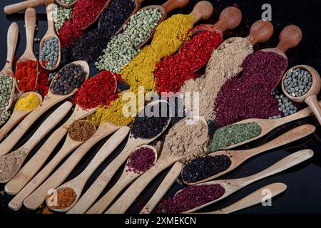 Große Sammlung von Gewürzen und Kräutern in Holzlöffeln. Gewürze für Lebensmittel auf schwarzem Hintergrund. Bunte Kräuter und Gewürze zum Kochen Stockfoto