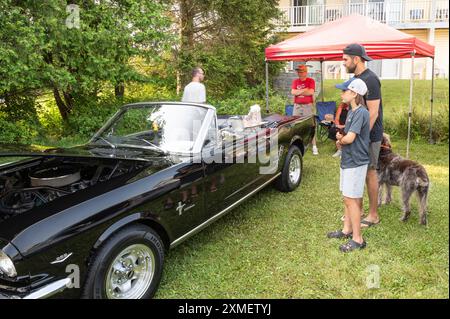 Hilton Beach, Ontario, Kanada - 27. Juli 2024: Ford Mustang Cabrio 1966 schwarz auf der Classic Car Show. Vater und Sohn suchen nach Einem A&W-Retro-Fenster. Stockfoto