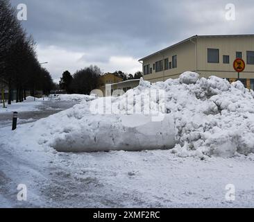 Dieses Bild zeigt einen beträchtlichen Schneehaufen, der sich im Winter in einem Vorort angesammelt hat. Die Szene zeigt einen bewölkten Himmel, ein Wohngebäude Stockfoto