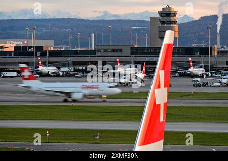 Vertikaler Stabilisator eines Airbus der Fluggesellschaft Swiss International Air Lines mit dem Schweizerkreuz, dahinter Ein Flugzeug der Swiss Airlines, das nach Ta fährt Stockfoto