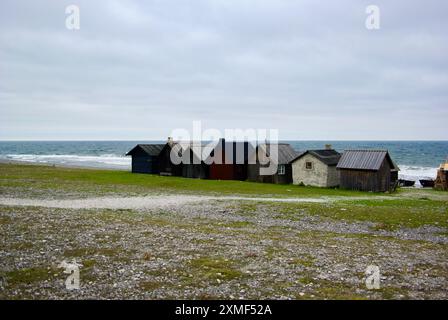 Kleine Fischerhütten in einer Reihe und einige Holzboote in einem alten Fischerdorf an der Ostsee auf der schwedischen Insel Fårö im Herbst. Stockfoto