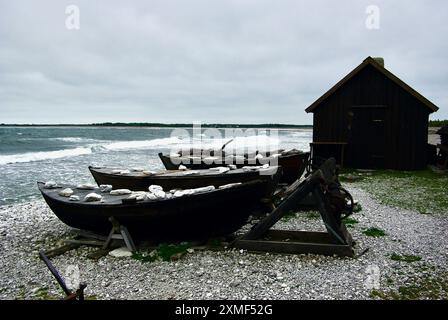 Kleines Fischerhäuschen hinter drei Holzbooten in einem alten Fischerdorf an der Ostsee auf der schwedischen Insel Fårö im Herbst. Stockfoto