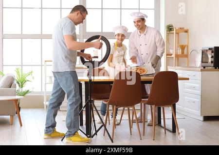 Glücklicher kleiner Junge mit seinem Vater und Großvater, der Kochvideo in der Küche aufnimmt Stockfoto