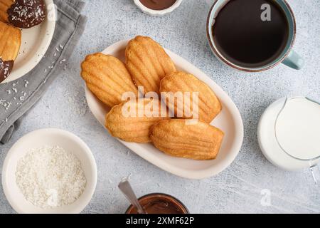 Teller mit köstlichen Madeleinen, Kokosflocken und einer Tasse Kaffee auf weißem Grunge Hintergrund Stockfoto