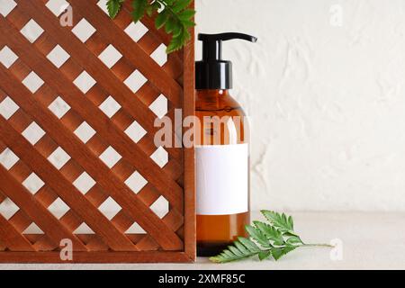 Flasche Kosmetik und Farnblätter in der Nähe des Holzgitters auf dem Lichttisch Stockfoto