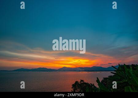 Lichtstrahlen der Sonne durchdrungen die bunten Wolken. Wunderbar die gelbe Sonne begann hinter der Insel zu erstrahlen. Das goldene Licht durchbohrte die SK Stockfoto