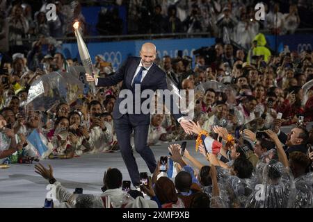 Paris, Frankreich. Juli 2024. Der Fußballmeister ZINEDINE ZIDANE trägt die Fackel bei der Eröffnungszeremonie der Olympischen Spiele 2024 in Paris im Regen. (Kreditbild: © Mark Edward Harris/ZUMA Press Wire) NUR REDAKTIONELLE VERWENDUNG! Nicht für kommerzielle ZWECKE! Stockfoto