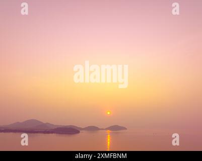 Aus der Vogelperspektive strahlten Lichtstrahlen der Sonne in die bunten Wolken ein. Wunderbar die gelbe Sonne begann hinter der Insel zu erstrahlen. Das goldene Licht pi Stockfoto