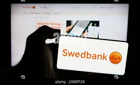 Person mit Smartphone und Logo des schwedischen Finanzdienstleisters Swedbank ab vor der Website. Schwerpunkt auf dem Display des Telefons. Stockfoto