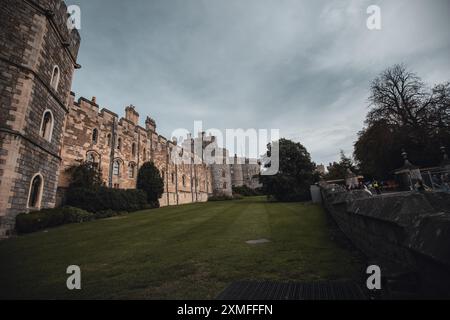 Windor Castle, Großbritannien - 16. Oktober 2023 : Eine Burgmauer aus Stein mit kleinen Fenstern überblickt ein grasbewachsenes Feld und ein Metallgitter. Stockfoto