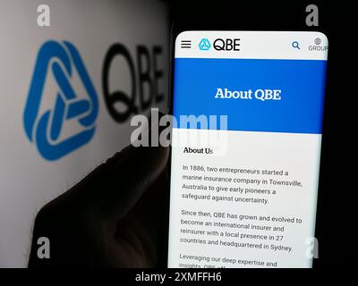 Person, die ein Mobiltelefon hält, mit Webseite der australischen QBE Insurance Group Limited vor dem Logo. Konzentrieren Sie sich auf die Mitte des Telefondisplays. Stockfoto
