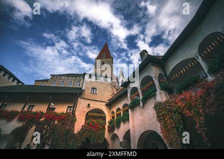 Österreich - 26. Oktober 2023 : die alte Architektur Einer europäischen Stadt zeigt rote Blumen, Weinstöcke, Mais und einen hohen Turm unter einem bewölkten blauen Himmel. Stockfoto